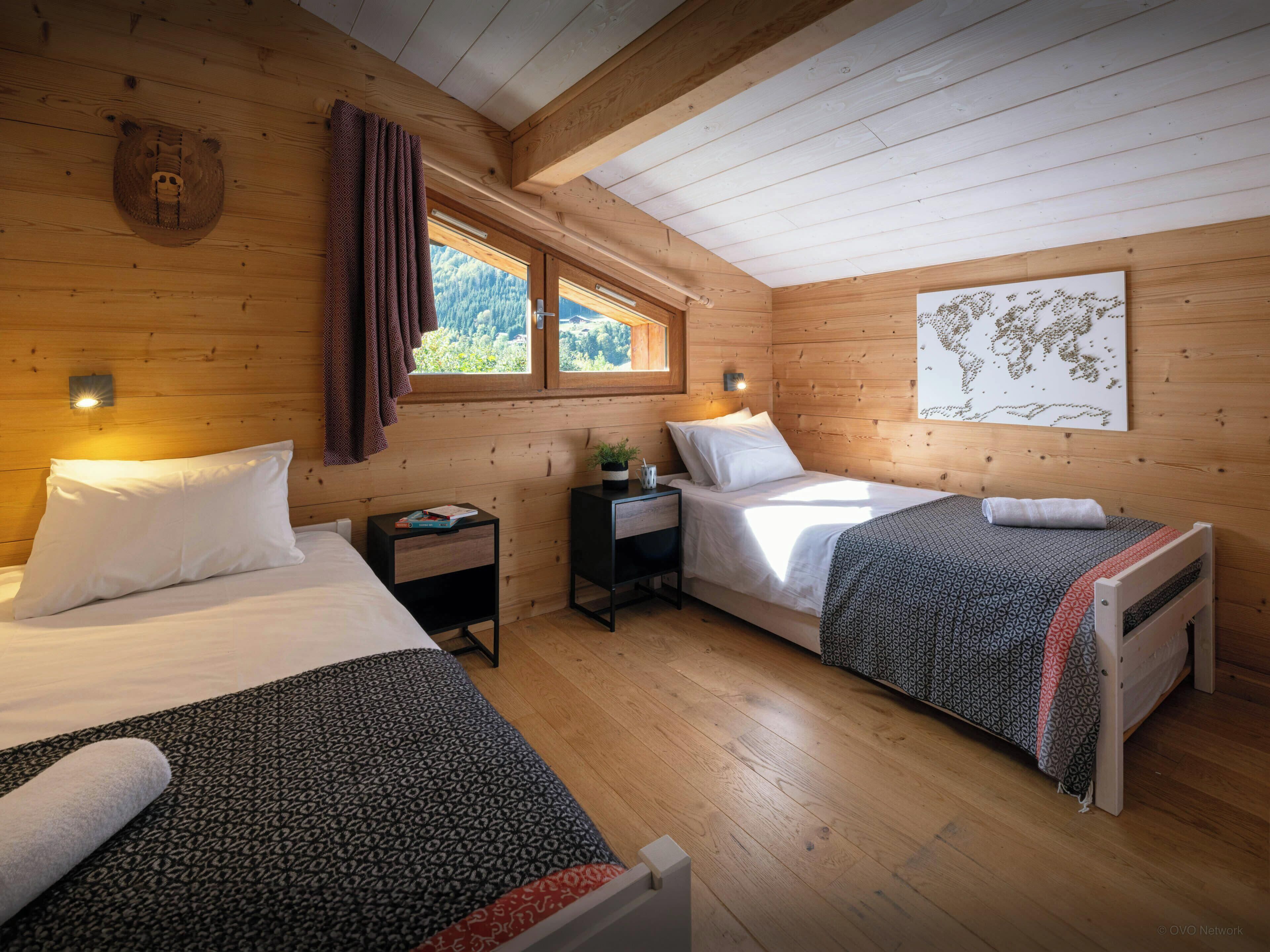 A cozy cabin room with two beds, wooden walls, a large window, and a world map on the wall.