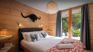 A bedroom with a wooden wall, a bed with white bedding, a red and white blanket, and a mounted animal head. - Chalet Paravis - La Clusaz stay for 9 sauna and games room - OVO Network (La Clusaz)