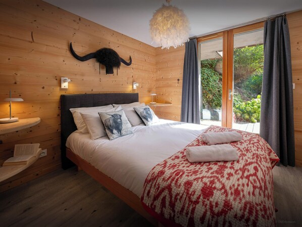 A bedroom with a wooden wall, a bed with white bedding, a red and white blanket, and a mounted animal head.