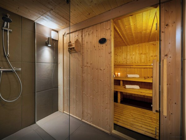 Una sauna de madera con puerta de vidrio, zona de ducha y estante con toallas.
