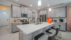 A modern kitchen with white cabinets, a large island with bar stools, and a microwave above the counter.