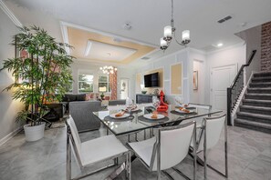 A modern dining area with a glass table, white chairs, and a large potted plant.