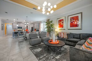 A modern living room with grey sofas, a coffee table, and a dining area with a kitchen in the background.
