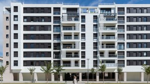 Un edificio residencial de varios pisos con balcones, una entrada central y un cielo despejado.