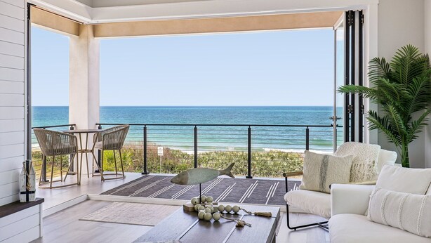 Uma varanda com vista para o oceano, uma mesa com cadeiras e um sofá branco.