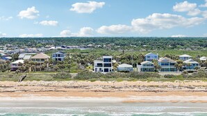 Uma área residencial costeira com propriedades em frente ao mar, incluindo casas modernas com amplas janelas e varandas, uma praia de areia e vista para o oceano.