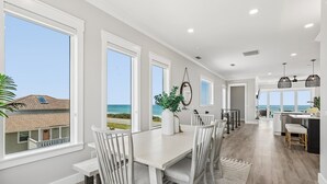 Uma sala de jantar espaçosa com vista para o mar, uma cozinha com balcão e uma grande janela.