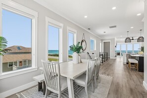 Un comedor amplio con vista al océano, una cocina con barra y un gran ventanal.