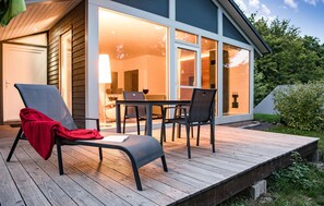 A wooden deck with a chair and table, a glass door leading to an interior space, and a view of a lake.