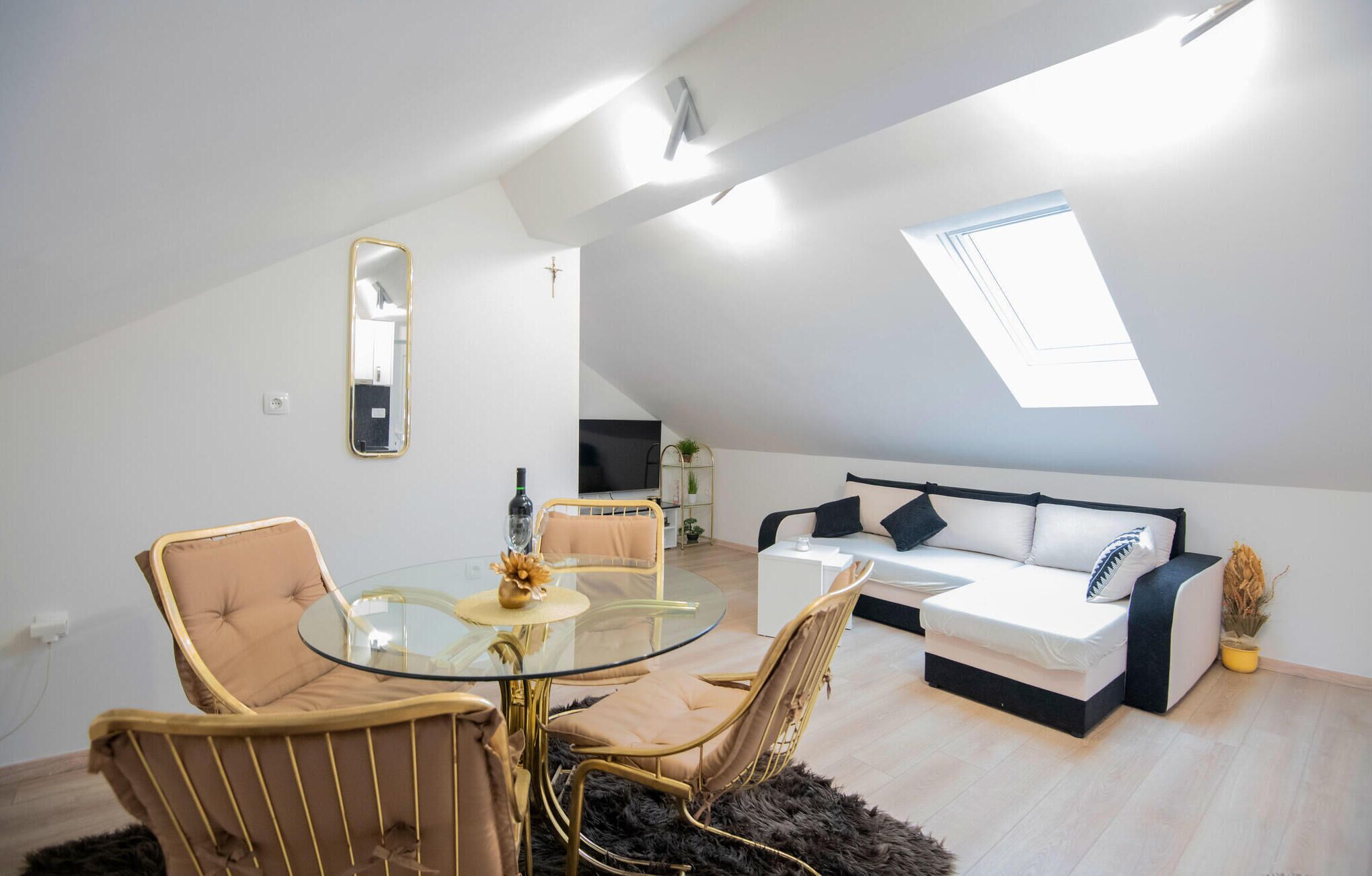 A modern loft apartment with a glass dining table, two sofas, a TV, and a skylight.