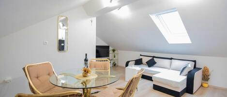 A modern loft apartment with a glass dining table, two sofas, a TV, and a skylight.