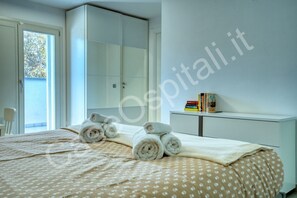 Habitació d'hotel amb llit, una taula de nit amb llibres, un armari i una finestra amb vistes.