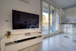 A modern living room with a flat-screen TV, a small plant, and a sliding glass door leading to a balcony.
