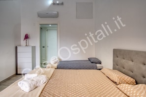 A hotel room with a bed, a bedside table, a lamp, and an air conditioning unit.