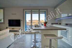 A modern kitchen with a central island, bar stools, a flat-screen TV, and a dining area with a view.