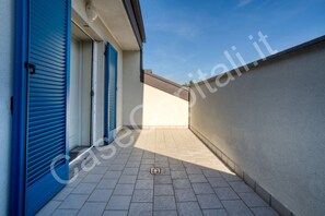 A narrow outdoor corridor with blue shutters, a tiled floor, and a clear sky.