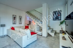 A modern living room with a sofa, a staircase, and artwork on the walls.
