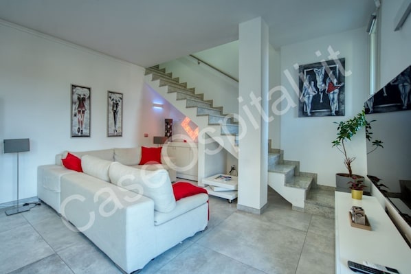 A modern living room with a sofa, a staircase, and artwork on the walls.