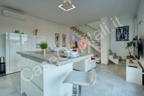 A modern kitchen with a central island, white cabinetry, and a staircase leading to another level.