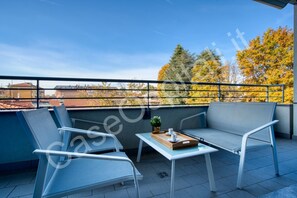 A balcony with a sofa, chairs, a table, and a tray with cups and saucers.