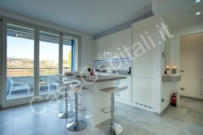 A modern kitchen with a central island, bar stools, and a view through large windows.
