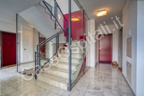 Un interior moderno con una escalera de cristal, una puerta roja y un suelo de baldosas.