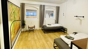 Ein Zimmer mit Holzboden, einem Bett, einer Bank, einem Sessel, einem kleinen Tisch und einem Heizkörper.
