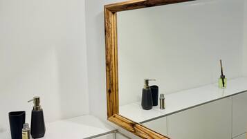 Ein Badezimmer mit einem großen Spiegel, weißen Fliesen, einem schwarzen Seifenspender, einer schwarzen Seife und einer kleinen Flasche auf der Ablagefläche.