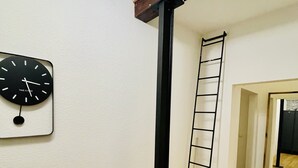 Ein Zimmer mit Holzboden, einer schwarzen Metallleiter und einer an der Wand befestigten Uhr.