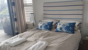 A large bed with white and blue patterned pillows, a headboard with horizontal stripes, and a window with blinds. - Wombarra Beach House with Ocean views 
Sleeps 8 (Wombarra)