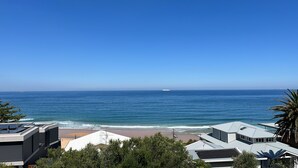 A coastal view with a beach, ocean, and modern buildings with flat roofs. - Wombarra Beach House with Ocean views 
Sleeps 8 (Wombarra)