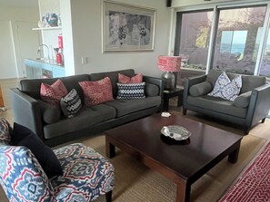 Un salon avec deux canapés, des coussins à motifs, une table basse et une fenêtre donnant sur un beau paysage.