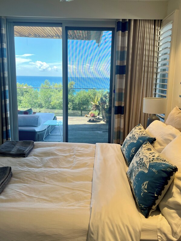 Une chambre d’hôtel avec un lit, une vue sur l’océan et un balcon aménagé avec du mobilier d’extérieur.