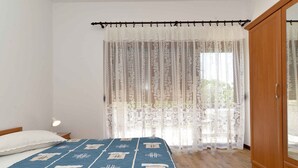 A bedroom with a bed, a wooden wardrobe, and a window with sheer curtains.