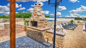 An outdoor patio with a stone barbecue, lounge chairs, and a pool.