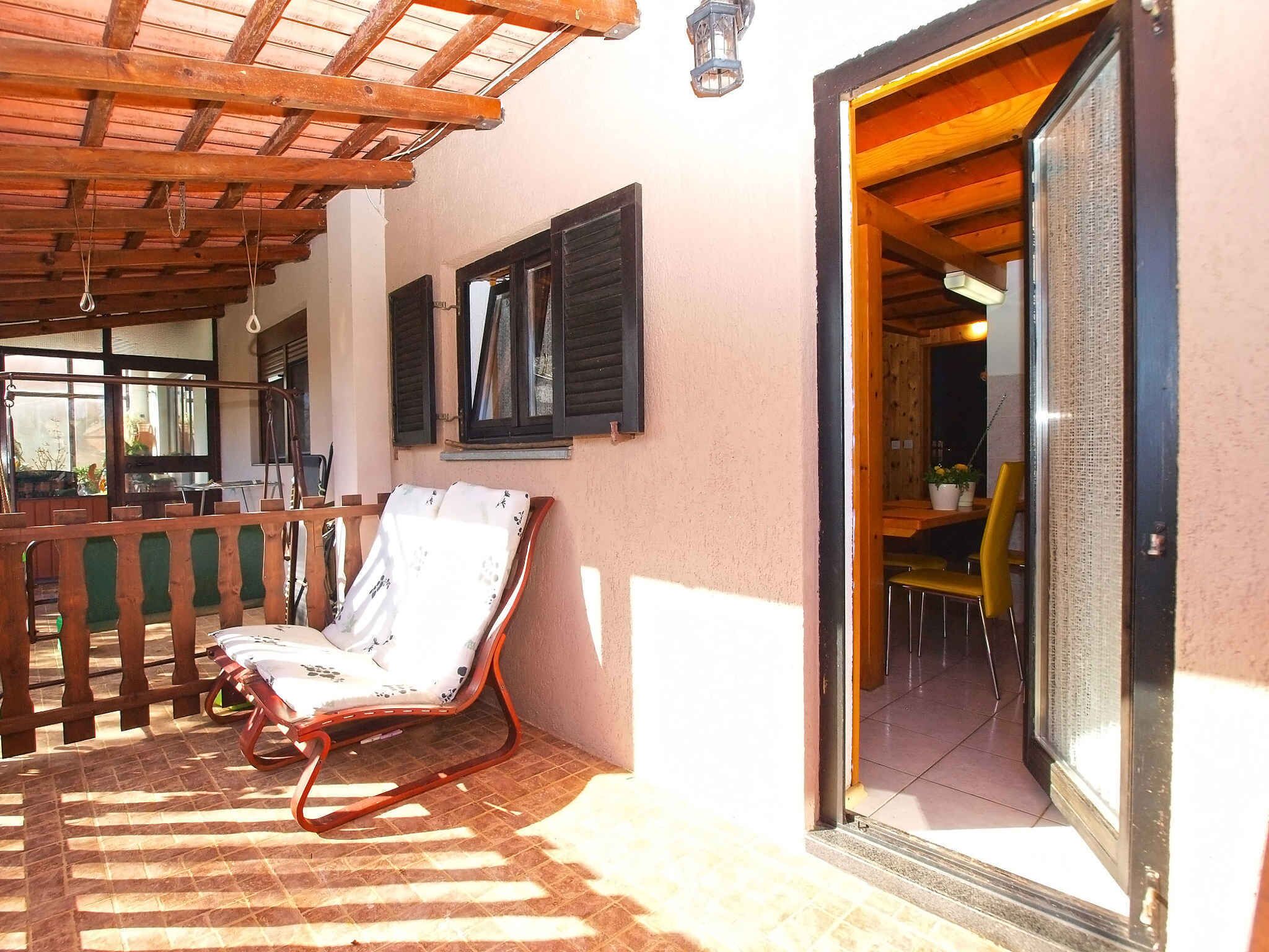 A wooden deck with a chair, a wooden railing, and a door leading to an interior space.