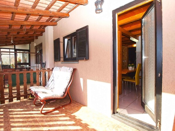 A wooden deck with a chair, a wooden railing, and a door leading to an interior space.