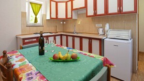 Una cocina compacta con una mesa de comedor preparada para dos personas, un refrigerador y una ventana con cortinas.