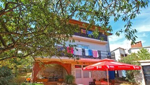 A two-story building with a patio area featuring outdoor seating and a red umbrella. - Holiday apartment with air conditioning and barbecue facilities (Premantura)