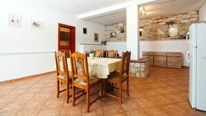 A dining area with a table and chairs, a kitchen with a refrigerator, and a stone wall. - Holiday apartment with air conditioning and barbecue facilities (Premantura)
