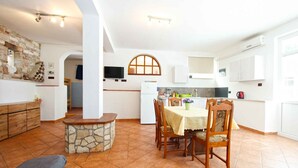A spacious living area with a stone fireplace, a dining table with chairs, and a kitchen area with white cabinets and a microwave. - Holiday apartment with air conditioning and barbecue facilities (Premantura)