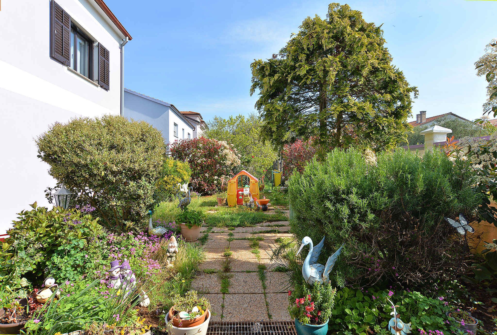 A garden pathway leading to a small playhouse, surrounded by lush greenery and various potted plants.