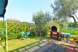 A patio with a swing set, a barbecue grill, and a small table.