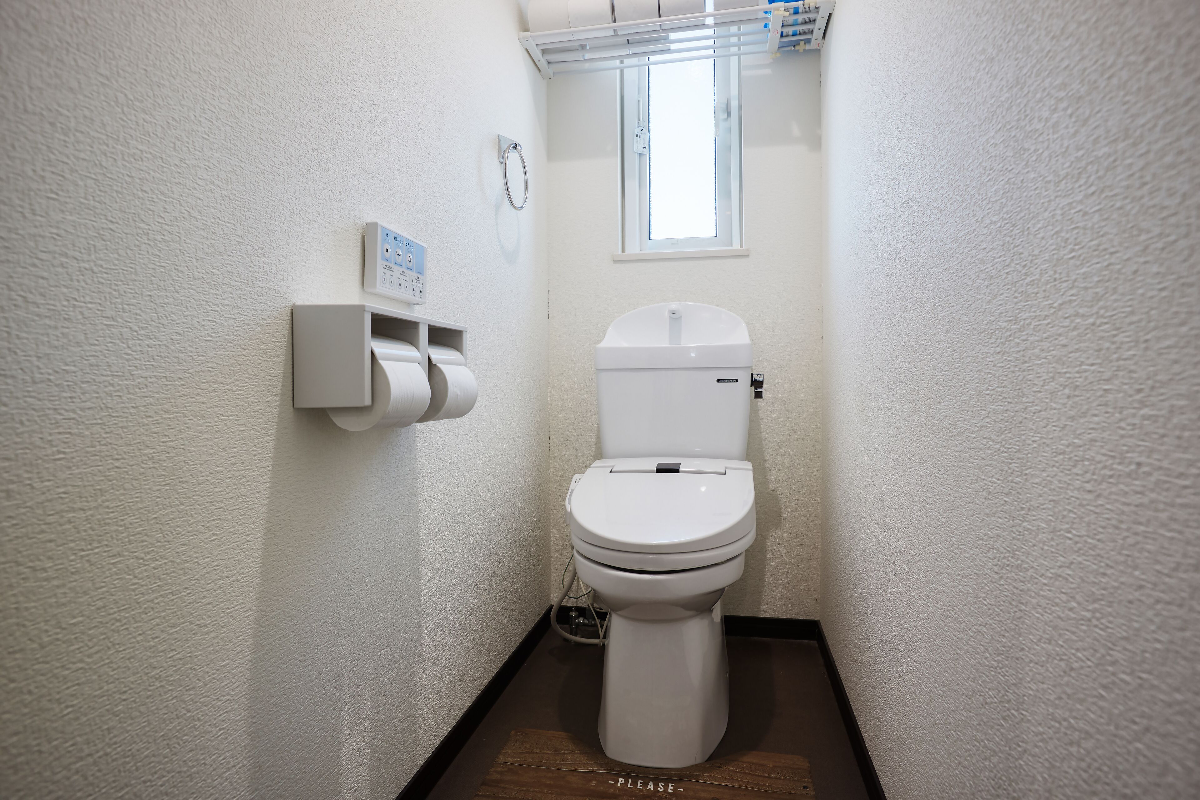 A small, clean bathroom with a toilet, a toilet paper holder, and a window.