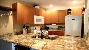A kitchen with granite countertops, wooden cabinets, a white refrigerator, and a coffee maker. - Beautiful 2 bedroom, 2 bath Condo in Maui Hawaii! Maui Kamaole C204. South Kihei (Kihei)