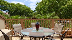 A round glass table with woven chairs and a vase, surrounded by lush greenery and a wooden fence. - Beautiful 2 bedroom, 2 bath Condo in Maui Hawaii! Maui Kamaole C204. South Kihei (Kihei)