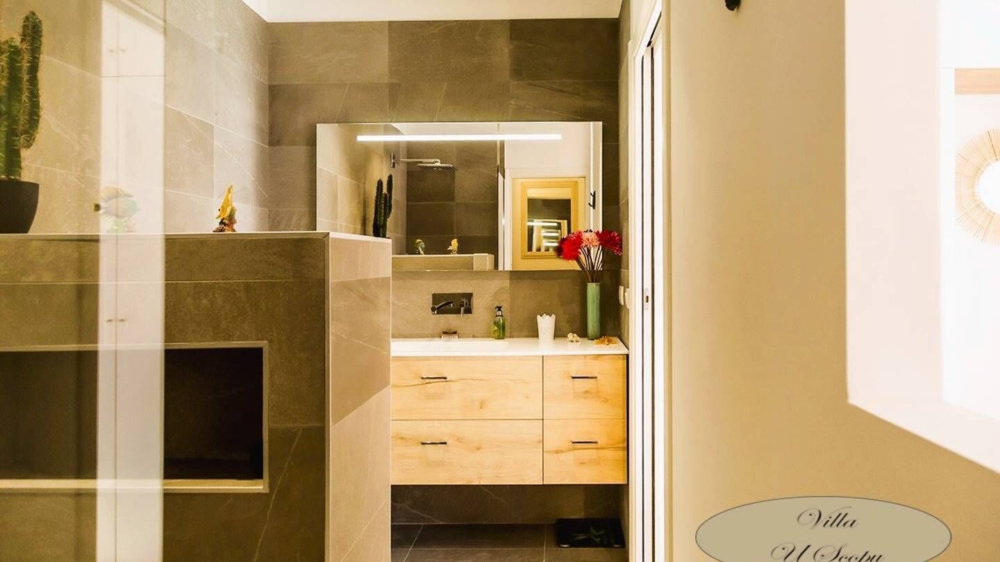 A modern bathroom with a large mirror, a shower, and a vanity with wooden drawers.