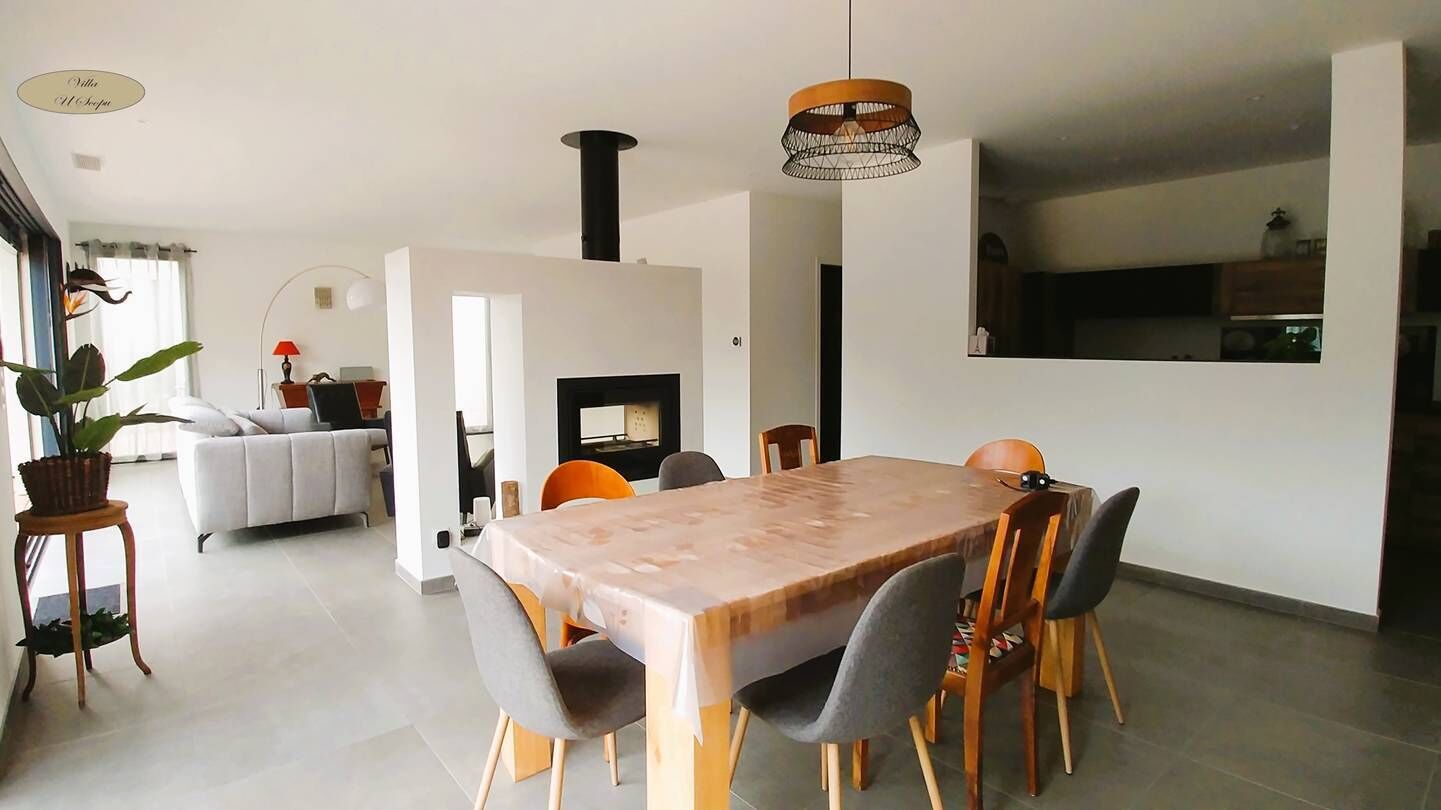 Un comedor moderno con una mesa y sillas de madera, una chimenea y una cocina al fondo.