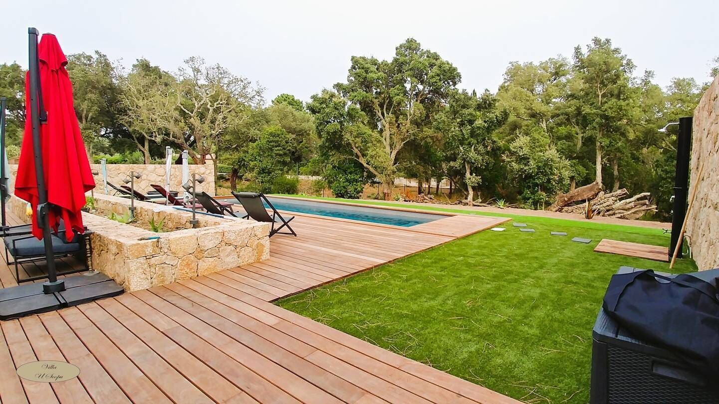 A wooden deck with a pool, a stone planter, and a red umbrella.