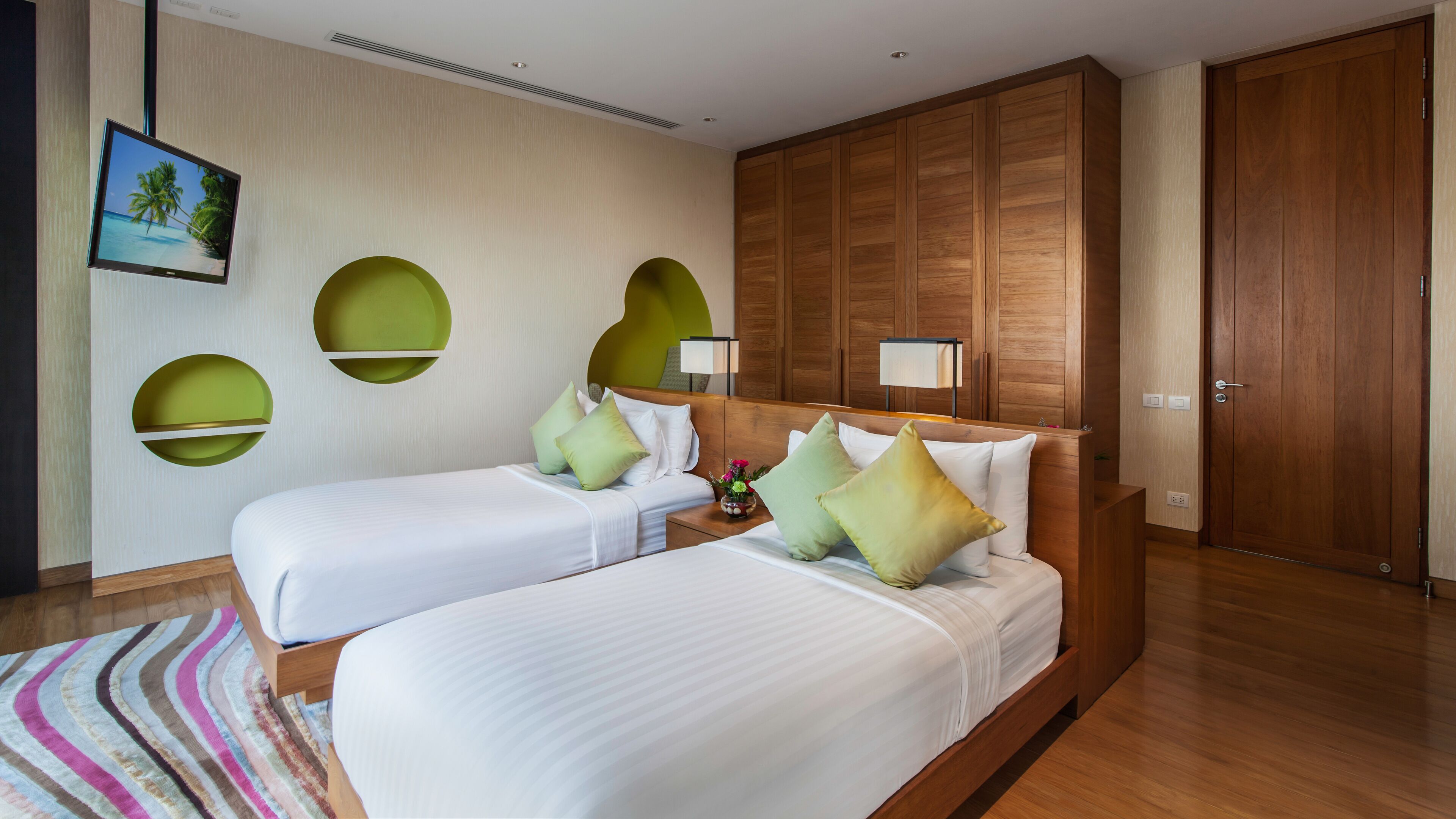 A hotel room with two beds, a wooden wardrobe, a wall-mounted TV, and a decorative wall panel.